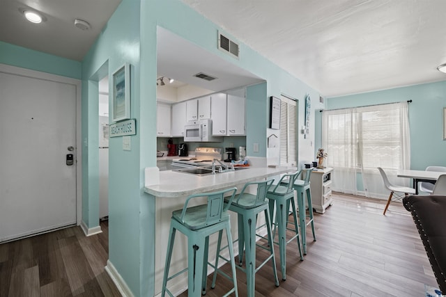 kitchen featuring a kitchen breakfast bar, hardwood / wood-style floors, white appliances, and white cabinetry