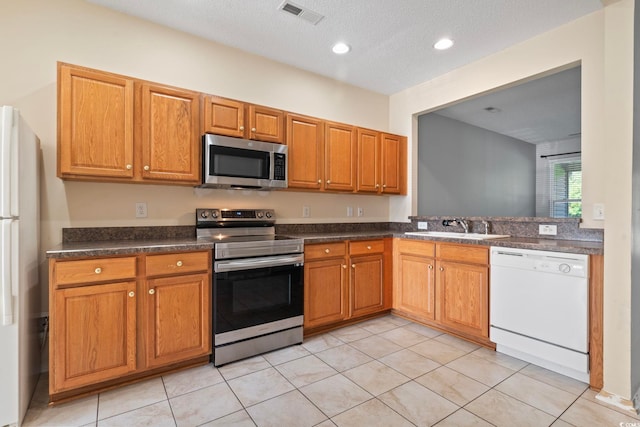 kitchen with light tile patterned floors, a textured ceiling, appliances with stainless steel finishes, and sink