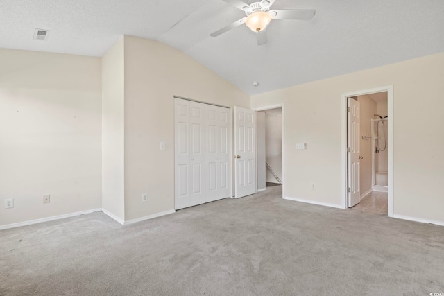 unfurnished bedroom with ceiling fan, ensuite bathroom, a closet, light colored carpet, and vaulted ceiling