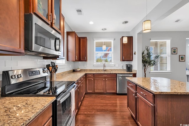 kitchen featuring light stone counters, dark hardwood / wood-style floors, sink, decorative light fixtures, and stainless steel appliances