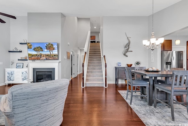 dining area with dark wood-type flooring, a towering ceiling, and ceiling fan with notable chandelier