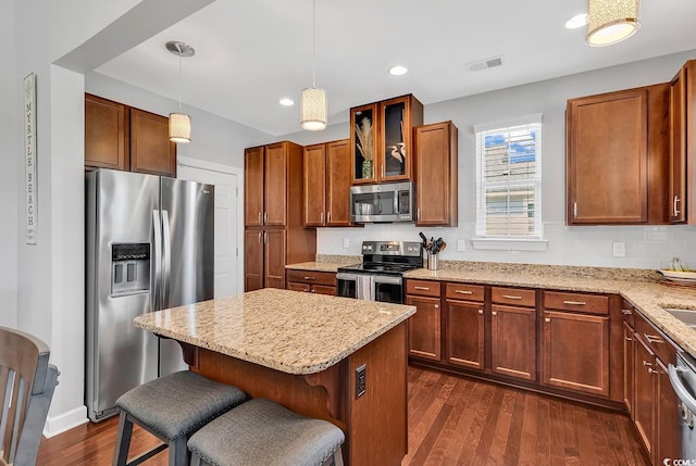 kitchen with a breakfast bar, decorative light fixtures, appliances with stainless steel finishes, light stone counters, and dark hardwood / wood-style flooring