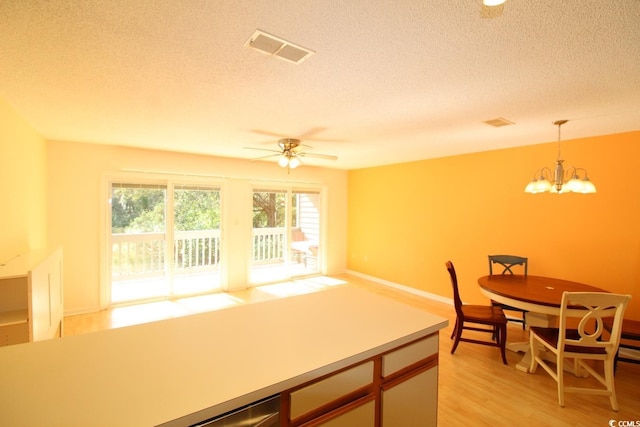 kitchen with light wood-type flooring, ceiling fan with notable chandelier, a textured ceiling, and decorative light fixtures