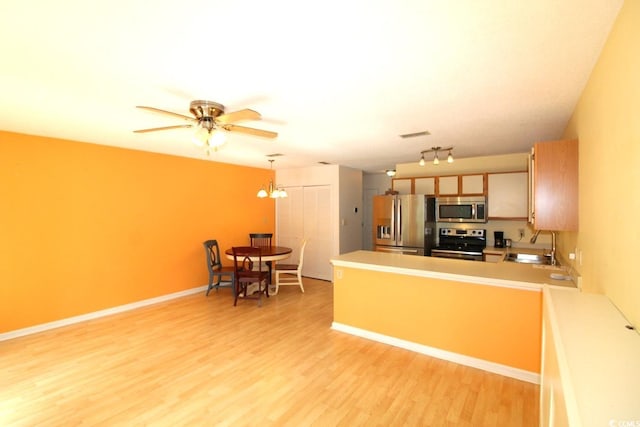 kitchen with stainless steel appliances, sink, kitchen peninsula, ceiling fan with notable chandelier, and light hardwood / wood-style flooring