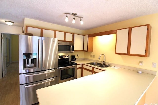 kitchen with appliances with stainless steel finishes, a textured ceiling, sink, hardwood / wood-style flooring, and kitchen peninsula