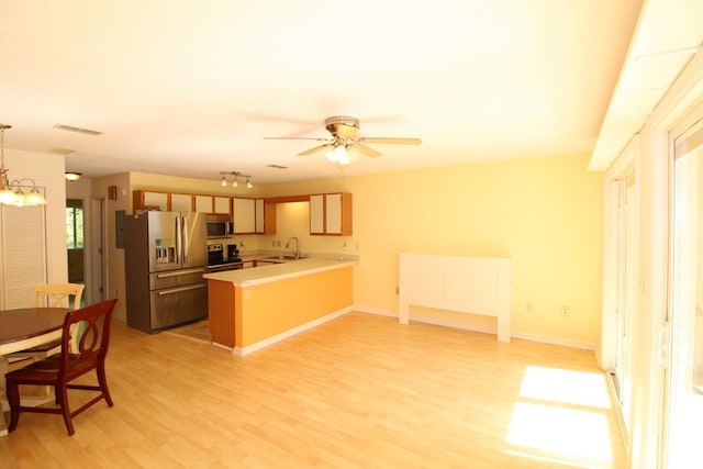 kitchen featuring appliances with stainless steel finishes, hanging light fixtures, sink, light hardwood / wood-style floors, and kitchen peninsula