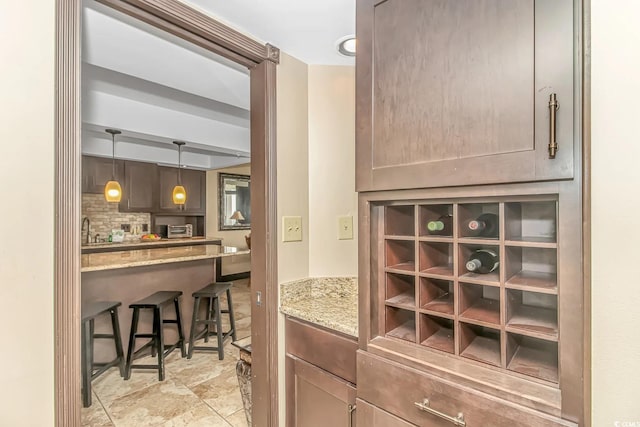 interior space with decorative backsplash, a kitchen breakfast bar, light stone countertops, and hanging light fixtures