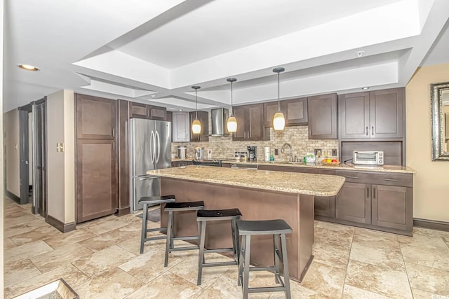 kitchen with decorative light fixtures, stainless steel fridge, wall chimney exhaust hood, a kitchen breakfast bar, and a kitchen island