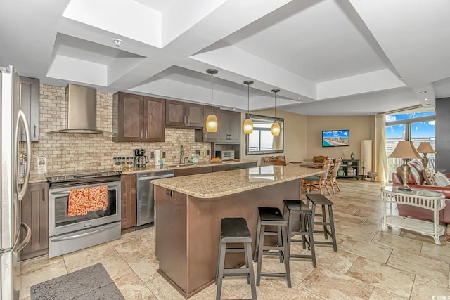 kitchen featuring a breakfast bar area, light stone countertops, appliances with stainless steel finishes, a center island, and wall chimney range hood