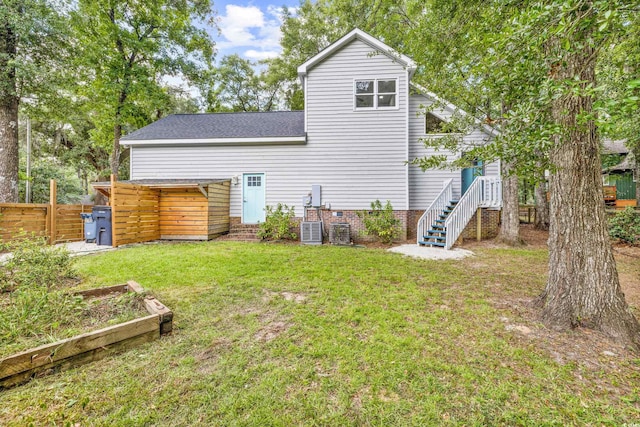 rear view of property featuring fence, a yard, central AC, a shingled roof, and a vegetable garden