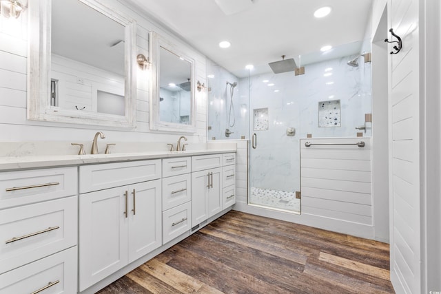 bathroom with double vanity, a sink, a marble finish shower, and wood finished floors