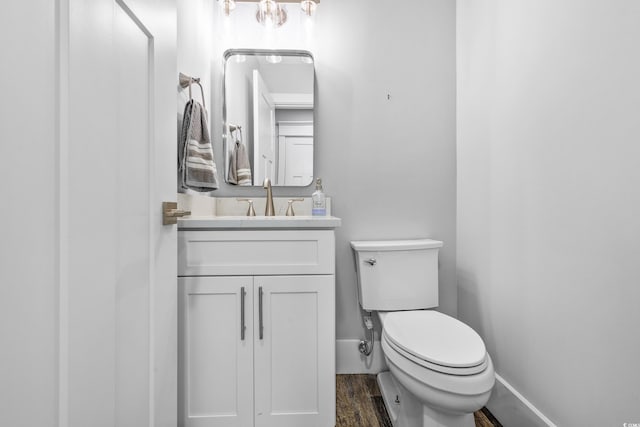 half bath with baseboards, wood finished floors, toilet, and vanity