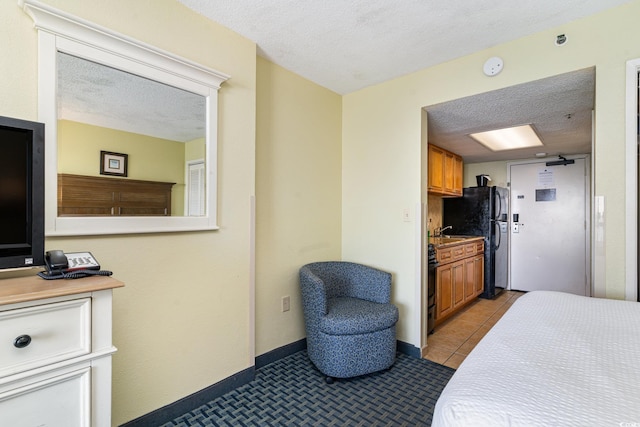 bedroom with a textured ceiling, black refrigerator, light tile patterned floors, and sink