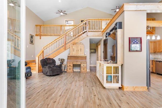 living room featuring a ceiling fan, high vaulted ceiling, light wood finished floors, and stairs