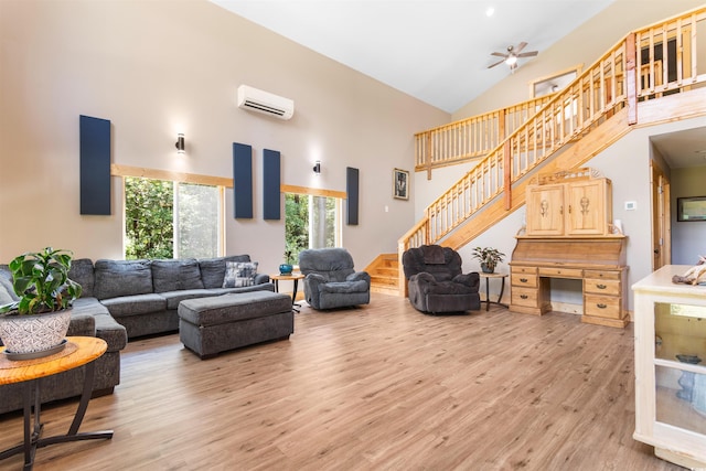 living room featuring a wall unit AC, ceiling fan, stairs, light wood-style floors, and high vaulted ceiling