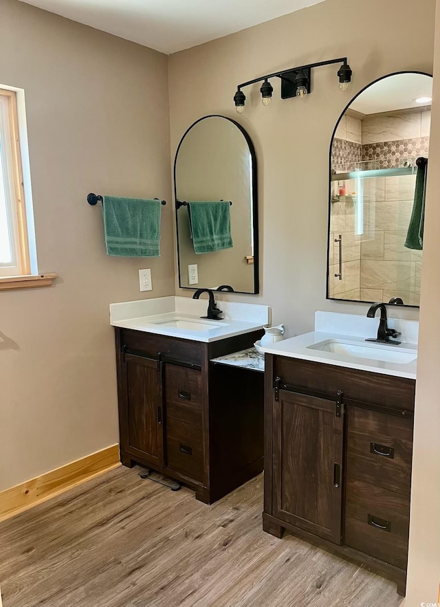 full bathroom featuring two vanities, a sink, a shower stall, and wood finished floors