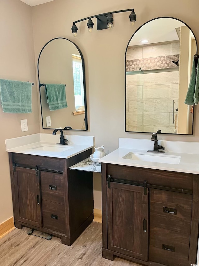 bathroom featuring two vanities, a sink, a tile shower, and wood finished floors