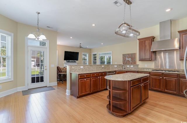 kitchen with kitchen peninsula, wall chimney exhaust hood, decorative light fixtures, a center island, and light wood-type flooring