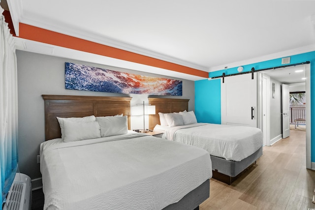 bedroom with a barn door, hardwood / wood-style flooring, and crown molding