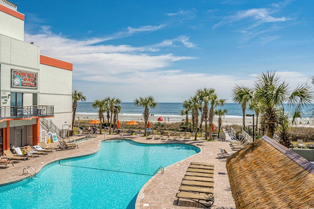 view of swimming pool featuring a patio area, a view of the beach, and a water view