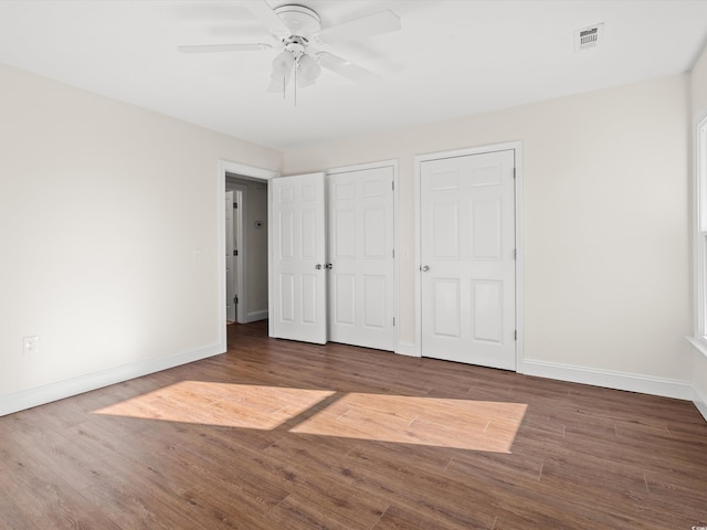 unfurnished bedroom featuring two closets, dark hardwood / wood-style flooring, and ceiling fan