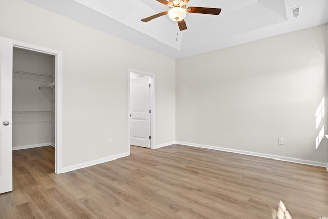 unfurnished bedroom featuring ceiling fan, a raised ceiling, a spacious closet, a closet, and light wood-type flooring