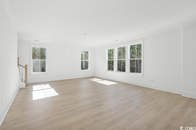 empty room with stairway, light wood-style flooring, baseboards, and ornamental molding