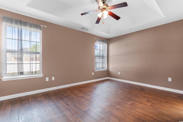 unfurnished room with dark wood-type flooring, a raised ceiling, and ceiling fan