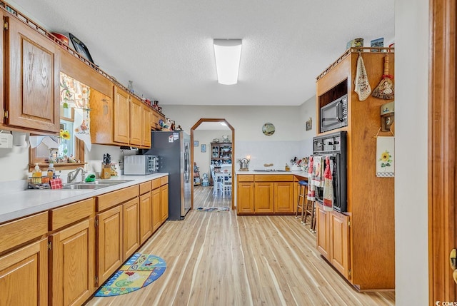 kitchen with arched walkways, light wood-style flooring, appliances with stainless steel finishes, light countertops, and a sink