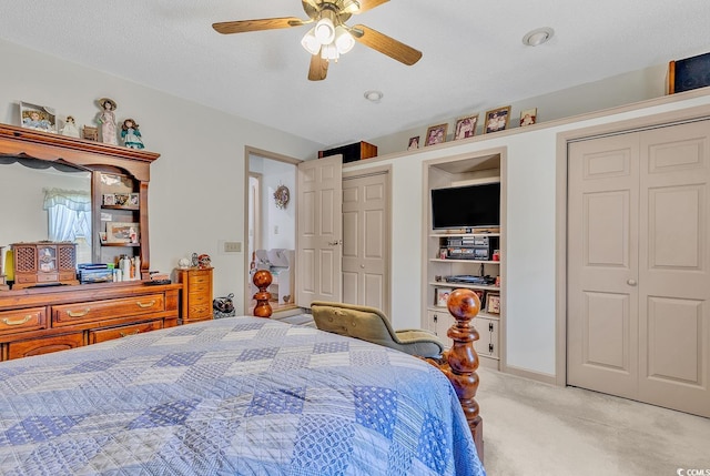 bedroom with ceiling fan, two closets, light colored carpet, and a textured ceiling