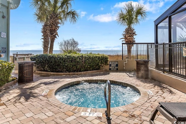 view of pool featuring glass enclosure, a water view, a patio area, and a hot tub