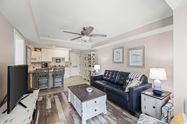 living room with light hardwood / wood-style flooring, ceiling fan, ornamental molding, and a tray ceiling