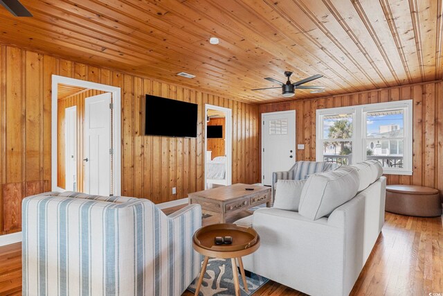 living room featuring wooden walls, light hardwood / wood-style flooring, wood ceiling, and ceiling fan