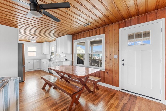 dining space featuring sink, wood ceiling, light hardwood / wood-style floors, ceiling fan, and wooden walls