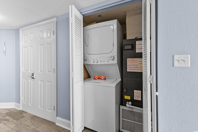 laundry area with a textured ceiling and stacked washer / dryer