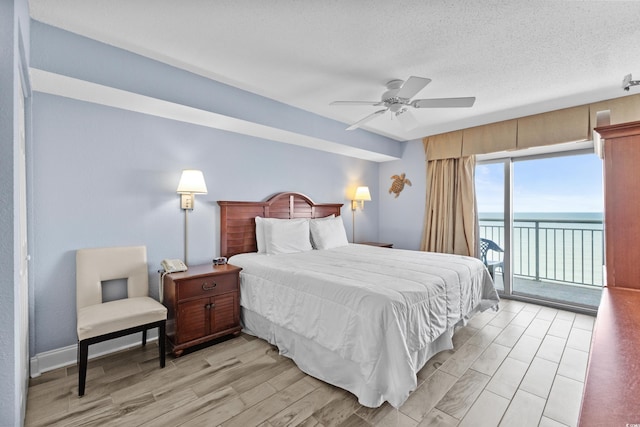 bedroom featuring ceiling fan, access to outside, a textured ceiling, light wood-type flooring, and a water view