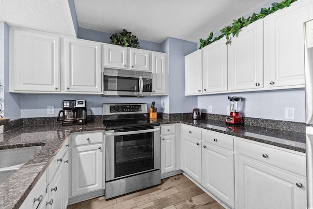 kitchen with dark stone counters, stainless steel appliances, white cabinetry, and light wood-type flooring