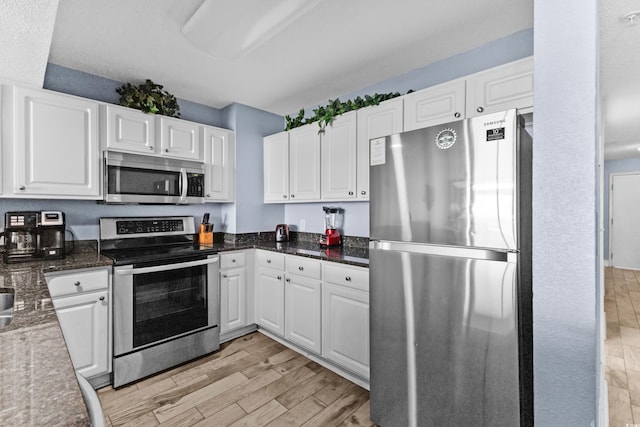 kitchen with dark stone countertops, stainless steel appliances, light hardwood / wood-style floors, and white cabinetry