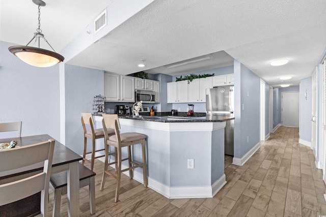 kitchen featuring light wood-type flooring, white cabinetry, kitchen peninsula, and appliances with stainless steel finishes