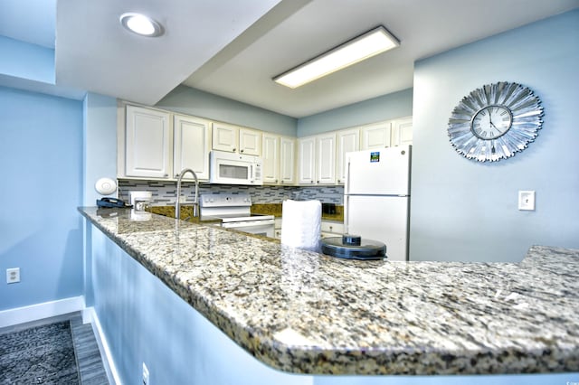 kitchen featuring dark stone countertops, hardwood / wood-style floors, white appliances, tasteful backsplash, and kitchen peninsula