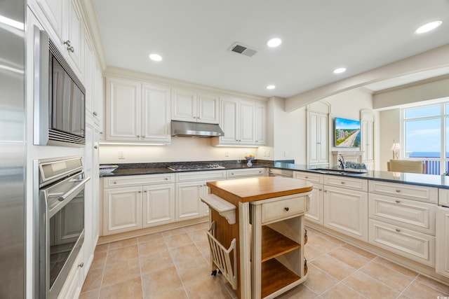 kitchen with kitchen peninsula, wood counters, sink, appliances with stainless steel finishes, and light tile patterned flooring