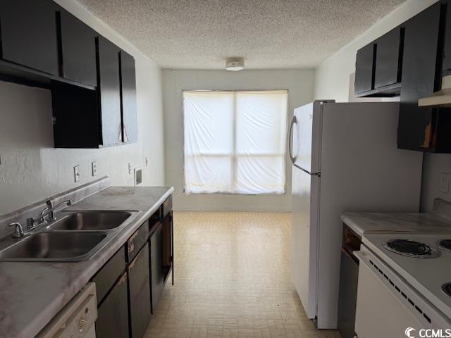 kitchen with dark cabinets, white appliances, a textured ceiling, and a sink