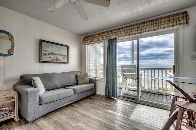 living area featuring a textured ceiling, ceiling fan, light wood-type flooring, and a water view