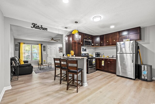 kitchen featuring ceiling fan, pendant lighting, light hardwood / wood-style flooring, stainless steel appliances, and a breakfast bar