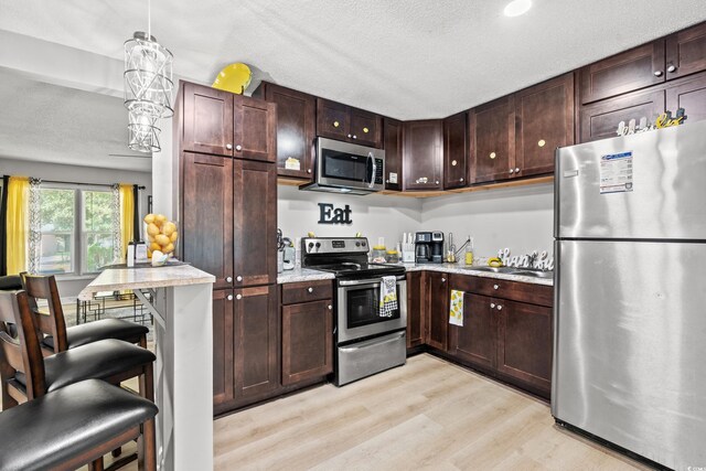 kitchen with a textured ceiling, sink, light hardwood / wood-style flooring, appliances with stainless steel finishes, and decorative light fixtures