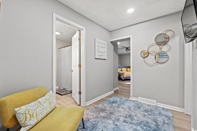 living area with ceiling fan, a textured ceiling, and light hardwood / wood-style floors