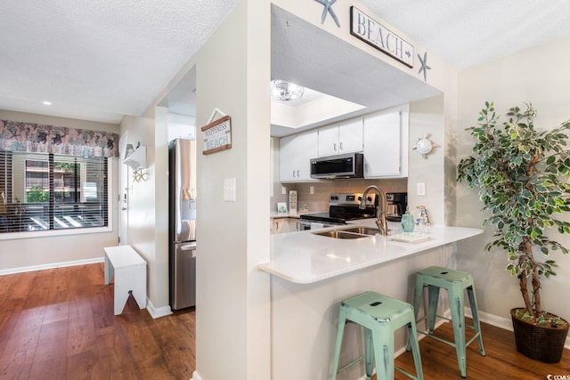 kitchen with white cabinetry, a kitchen bar, stainless steel appliances, decorative backsplash, and dark hardwood / wood-style floors