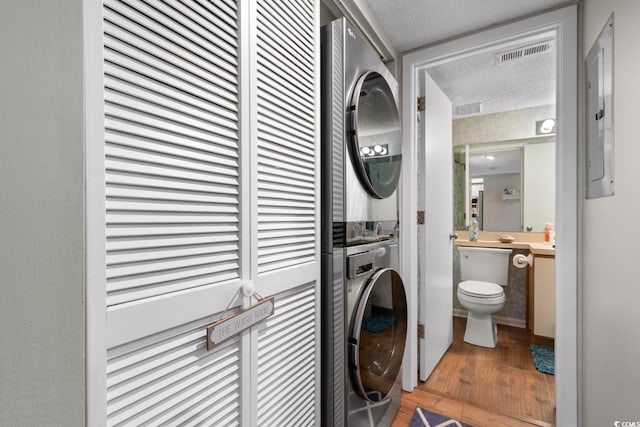 clothes washing area featuring wood-type flooring, stacked washer and clothes dryer, and a textured ceiling