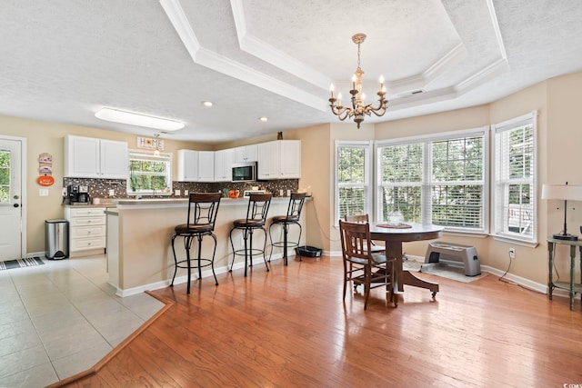 dining room featuring an inviting chandelier, a textured ceiling, light wood-type flooring, a raised ceiling, and ornamental molding