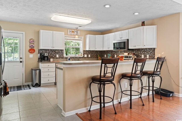 kitchen with white cabinets, light wood-type flooring, kitchen peninsula, and a kitchen breakfast bar